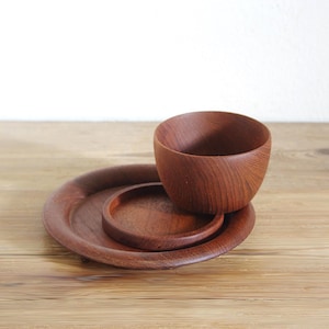 Op de afbeelding: Een set van drie bruine houten keukenartikelen bestaande uit een grote ronde plaat, een kleinere ronde onderzetter of deksel en een diepe ronde kom. De items hebben een zichtbare houtnerf en een gladde, gepolijste afwerking over het geheel.