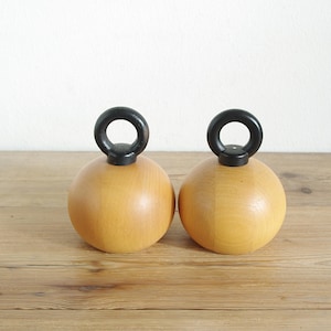 May include: Two wooden salt and pepper shakers with black handles. The shakers are round and have a light brown color.