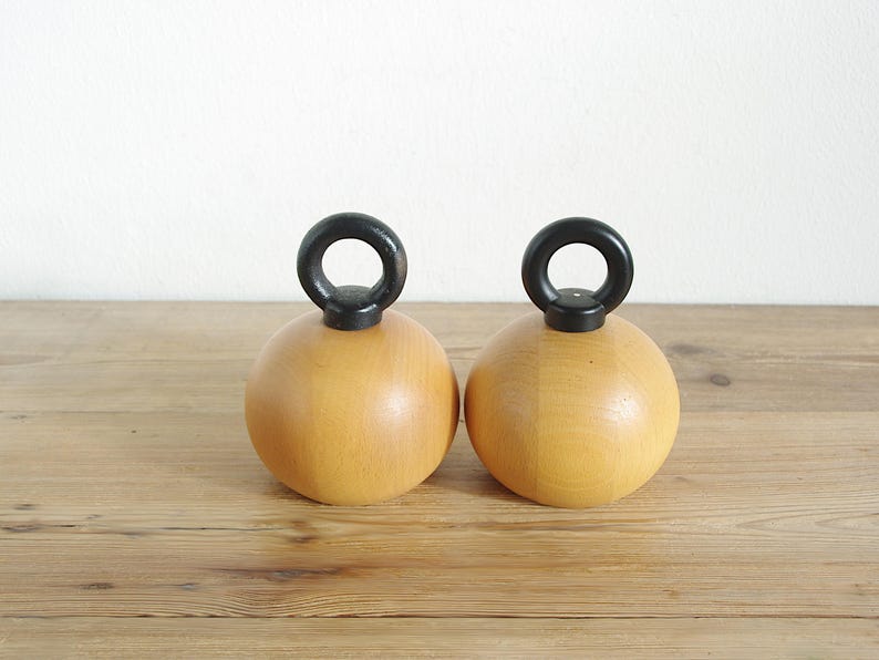 May include: Two wooden salt and pepper shakers with black handles. The shakers are round and have a light brown color.