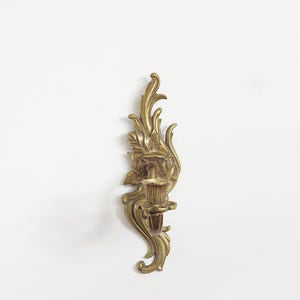 May include: Ornate brass wall sconce with a floral and leaf design. The sconce features a candle holder and decorative flourishes. The brass has a warm, aged patina. A classic piece for home decor.