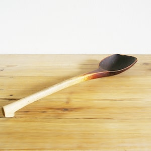 May include: A wooden spoon with a long, thin handle and a wide, rounded bowl. The spoon is dark brown in color and has a light brown handle.
