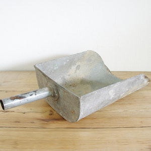 May include: A vintage metal scoop with a long handle. The scoop is made of galvanized metal and has a worn, rustic look.