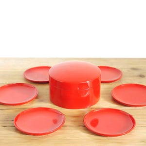 May include: A bright red circular lidded container sits in the center, surrounded by five matching small red circular plates. The set features a smooth, glossy finish on all pieces, creating a uniform appearance across the entire collection.