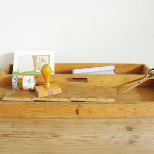 Könnte beinhalten: Ein Holztablett mit einem Griff, unterteilt in zwei Abschnitte. Das Tablett enthält einen Gummistempel, zwei Rollen Washi-Tape, ein Lineal und eine goldene Schere.