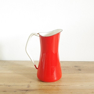 Może przedstawiać: Czerwony dzbanek emaliowany z białym wnętrzem i białym sznurkowym uchwytem. Dzbanek stoi na drewnianej powierzchni.