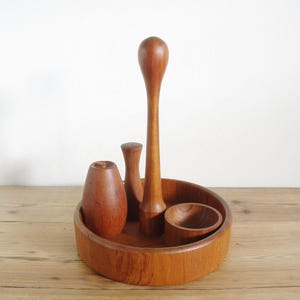 Może przedstawiać: Drewniany stojak na pierścionki z czterema przegródkami. Stojak wykonany jest z ciemnobrązowego drewna i ma okrągłą podstawę. Są trzy wysokie, wąskie przegródki i jedna mała, okrągła przegródka.