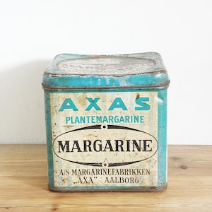 Peut inclure: Boîte de margarine AXAS vintage avec un couvercle et des côtés turquoise. La boîte présente les mots "AXAS PLANTE-MARGARINE" et "MARGARINE" dans un design ovale audacieux. Le bas de la boîte indique "A/S MARGARINEFABRIKKEN 'AXA' AALBORG."