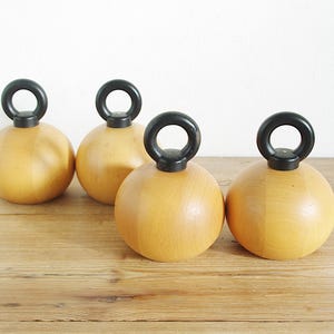 May include: Four wooden salt and pepper shakers with black handles. The shakers are round and have a light wood color.