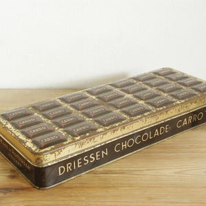 Peut inclure: Une boîte en métal vintage pour DRIESSEN CHOCOLADE CARRO'S. La boîte est fabriquée à Rotterdam, en Hollande, et présente un motif de barres de chocolat avec le mot "CARRO" imprimé sur chaque barre.