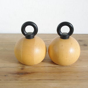 May include: Two wooden salt and pepper shakers with black handles. The shakers are round and have a smooth, natural wood finish.