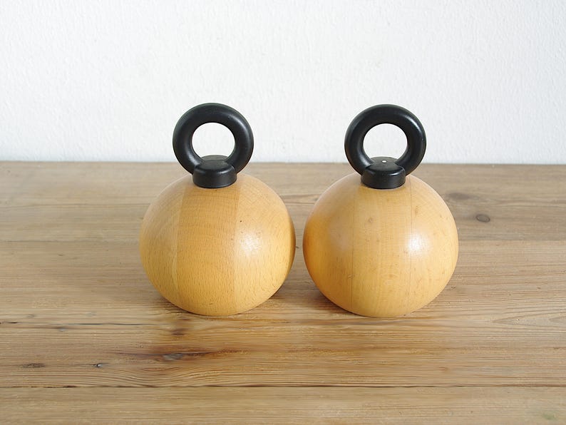 May include: Two wooden salt and pepper shakers with black handles. The shakers are round and have a smooth, natural wood finish.