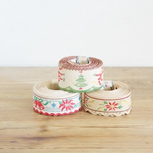 May include: Three rolls of vintage Christmas ribbon with festive designs. One roll features a Christmas tree, another has poinsettias and bells, and the third has floral patterns. The ribbons are beige with red, green, and blue accents.