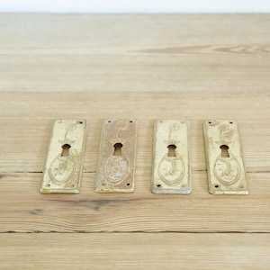 Op de afbeelding: Vier antieke messing sleutelgaten met sierlijke ontwerpen. Elk sleutelgat heeft een sleutelgat in het midden en is rechthoekig.