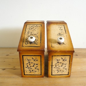 May include: Two wooden tea and coffee canisters with floral designs and white knobs. The canisters are labeled "Tea" and "Coffee" in a decorative script.
