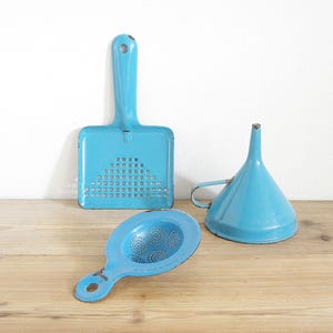 May include: Three blue enamel kitchen utensils: a colander, a funnel, and a sifter. The utensils are all made of metal and have a light blue enamel finish.