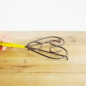 May include: A yellow metal hot pad with a heart-shaped design and a yellow plastic handle.