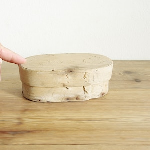 May include: A wooden box with a natural finish. The box is oval shaped and has a lid. The box is made of two pieces of wood that have been joined together.