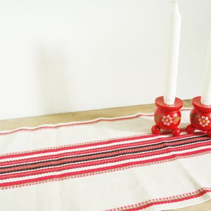 Könnte beinhalten: Zwei rote Kerzenhalter aus Holz mit weißen Kerzen und Blumendesigns auf einem weißen und roten gestreiften Tischläufer.