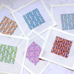Puede incluir: Seis cuadrados de lienzo blanco con un borde blanco, cada uno con un patrón de color diferente de arcos superpuestos con rayas verticales. Los patrones incluyen azul, verde, rosa, naranja, rojo y una combinación de azul claro y blanco.