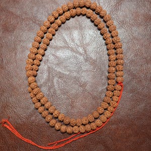 Pode incluir: Um colar de contas mala de madeira marrom com 108 contas e um tassel de corda vermelha.