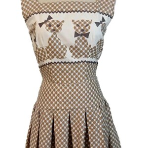 May include: A vintage dress with a brown and white checkered design. The bodice has a square neckline and a white panel with teddy bear illustrations. The pleated skirt and the dress is displayed on a mannequin.