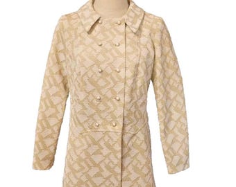 May include: A long-sleeved, cream-coloured coat with a geometric pattern and pearl-like buttons. The coat has a double-breasted closure and a collar.