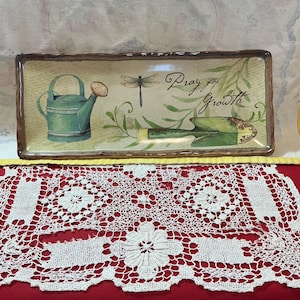 May include: Rectangular decorative tray with a brown border, featuring a garden theme. The tray has a green watering can, a dragonfly, and a trowel illustration. The text "Pray for Growth" is written on the tray.