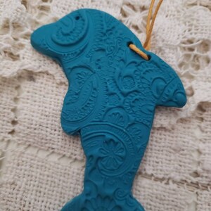 May include: A teal blue ceramic dolphin ornament with a paisley pattern. The dolphin has a hole at the top for hanging.
