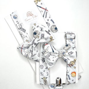 May include: White suspenders with a clip closure and a matching bow tie. Both feature a white background with a black and white doodle pattern of Star Wars characters and spaceships. The text "Feel the Force" and "May the Force be with you" are included in the pattern.