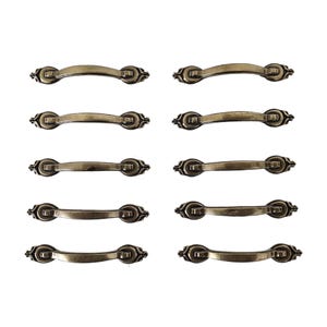 May include: A set of ten matching drawer pulls arranged in two vertical columns. Each pull is made of a metallic material with an antique brass finish, featuring a curved handle design and decorative circular mounting plates at both ends.