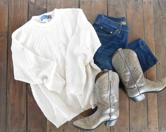 May include: A white knitted sweater, blue jeans, and a pair of brown cowboy boots.