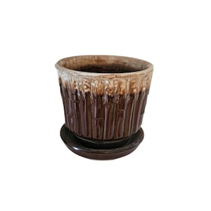 May include: A brown ceramic plant pot with a textured, vertical ribbed design. The top rim has a lighter, dripped glaze effect. The pot sits on a matching saucer, suitable for indoor or outdoor use. A decorative piece for plants.