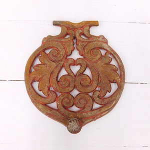 May include: A rusty metal decorative ornament with a red paint finish. The ornament features a detailed floral design with intricate swirls and leaves.