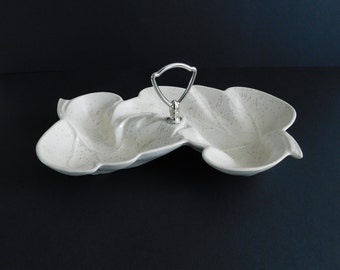 May include: A white ceramic serving dish with a silver handle. The dish is shaped like a leaf and has three sections.
