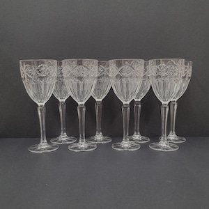Può includere: Set di otto bicchieri da vino in vetro trasparente con intricati disegni incisi. I bicchieri hanno un gambo alto e sottile e una coppa rotonda.