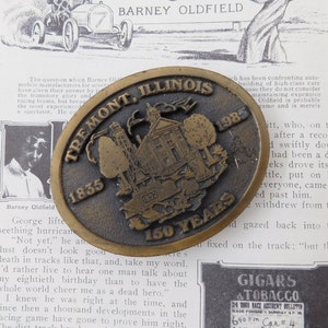 May include: A gold-colored metal belt buckle with a detailed image of a building and trees. The buckle is oval-shaped and has the text "Tremont, Illinois 1835 1892 150 Years" around the edge.