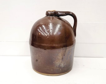 May include: A brown glazed stoneware jug with a handle and a lid. The jug has a rustic, vintage look.