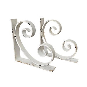 May include: A pair of white metal shelf brackets with a decorative scroll design. The brackets are distressed and have a vintage look.