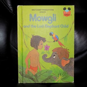 May include: A vintage hardcover book titled Mowgli and the Lost Elephant Child, featuring a light green cover with illustrations of Mowgli, a small elephant, and a colorful parrot. The text Walt Disney Productions presents is printed at the top.