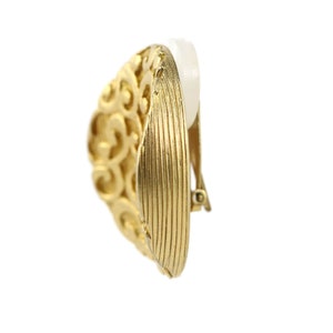 May include: Gold-toned clip-on earrings with a detailed filigree design. The earrings have a smooth, textured surface.