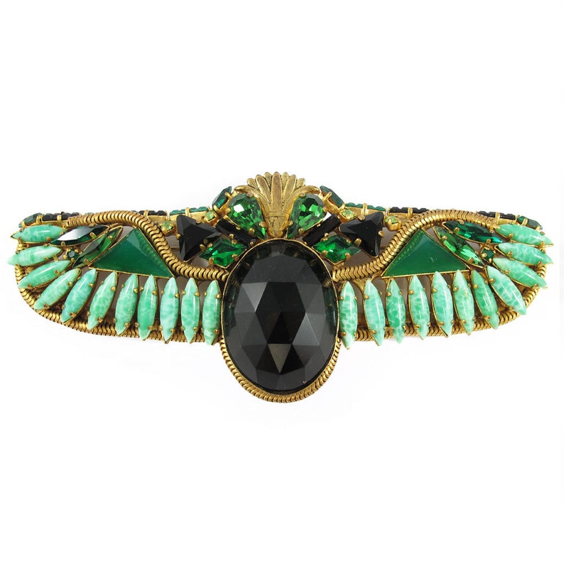 May include: A gold-toned brooch with a large black faceted stone surrounded by green and black rhinestones. The brooch is shaped like a winged scarab beetle.