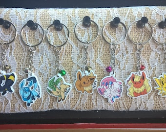 May include: A set of 10 keychains featuring different Pokemon characters. Each keychain has a silver ring and a small charm attached to it. The charms are made of colorful plastic and depict various Pokemon, including Eevee, Flareon, Jolteon, Vaporeon, Espeon, Umbreon, Leafeon, Glaceon, Sylveon, and  a blue and green water Pokemon.