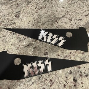 May include: Two black pennant flags with the word "KISS" printed in white on each. The flags are made of a thick, black material and have a hole at the top for hanging.