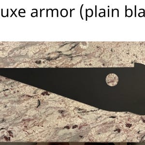 May include: A black, triangular-shaped armor piece with a round hole in the center. The armor is made of a thick, durable material and is designed to protect the wearer from harm. The armor is shown on a granite countertop.