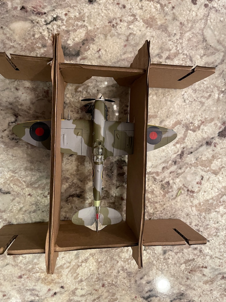 May include: A model of a green, gray, and brown camouflage World War II era fighter plane with red and white markings. The plane is in a cardboard box.