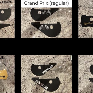 May include: A collection of black pinball machine side rails with various designs. The designs include a yellow hazard symbol, checkered flags, a sword, the text "NASCAR", and a red "R" logo. The text "The Simpsons Pinball Party deLuxe", "Grand Prix (regular)", and "Lord of the Rings LE (deluxe)" are also visible.