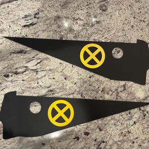 May include: Two black triangular-shaped vinyl decals with a yellow X-shaped symbol in a circle. The decals have a round hole in the top corner.