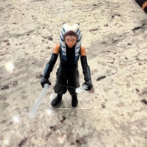 以下が含まれることがあります： アソーカ・タノのスターウォーズアクションフィギュア。特徴的な頭部のテールとレックが特徴です。フィギュアは黒い衣装を着て、2本のライトセーバーを持っています。フィギュアは透明なプラスチックベースに立っています。コレクションアイテムです。