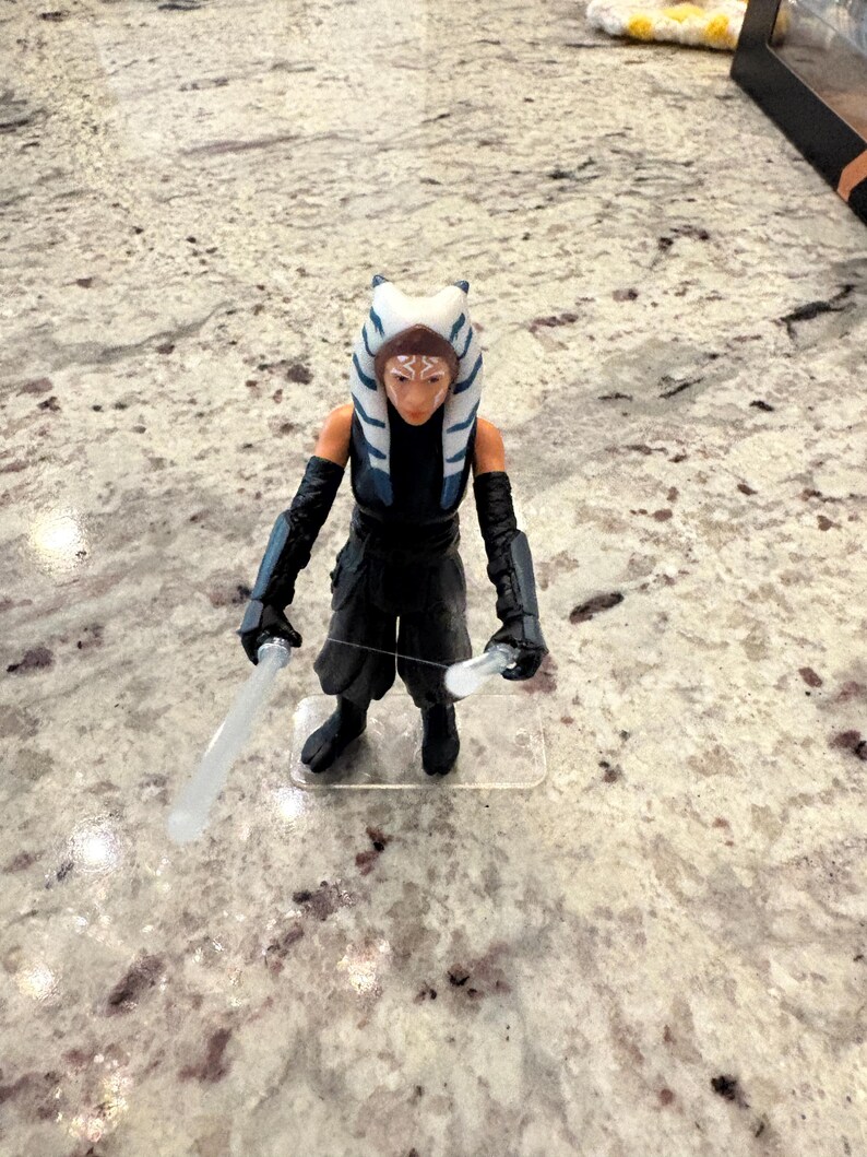 以下が含まれることがあります： アソーカ・タノのスターウォーズアクションフィギュア。特徴的な頭部のテールとレックが特徴です。フィギュアは黒い衣装を着て、2本のライトセーバーを持っています。フィギュアは透明なプラスチックベースに立っています。コレクションアイテムです。