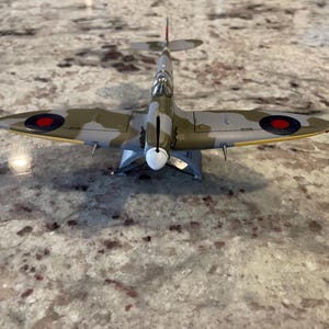 May include: A detailed model of a British Supermarine Spitfire fighter plane with a camouflage paint scheme of green, brown, and gray. The plane has red, white, and blue roundels on the wings.